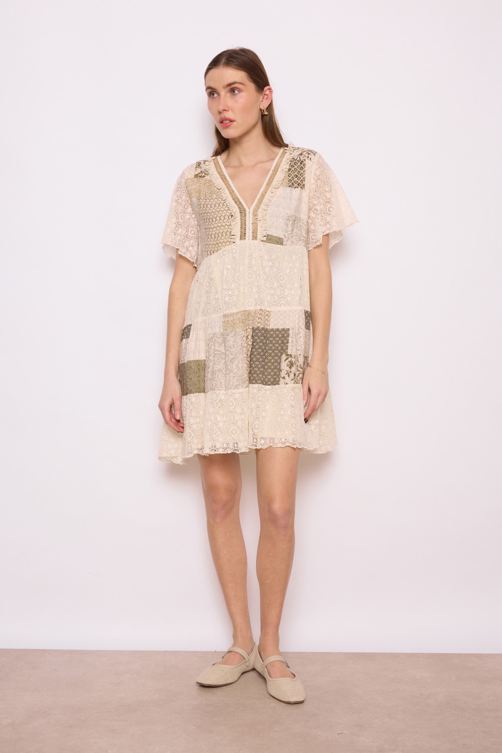 Réf. 41002 - Robe en dentelle patchwork, combinant différentes textures et motif dans des couleurs neutres. Décolleté plongeant en V et des manches courtes légèrement évasées, elle dégage un charme bohème et féminin. La robe s'évase en une jupe ample à volants, ce qui crée une silhouette gracieuse et aérienne. C'est une tenue parfaite pour les événements printaniers ou estivaux, alliant élégance et confort.