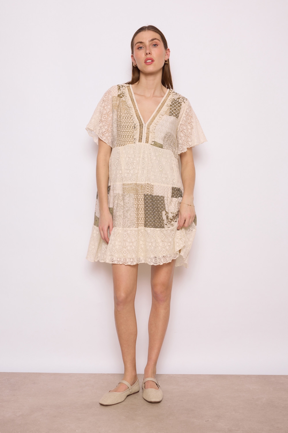 Réf. 41002 - Robe en dentelle patchwork, combinant différentes textures et motif dans des couleurs neutres. Décolleté plongeant en V et des manches courtes légèrement évasées, elle dégage un charme bohème et féminin. La robe s'évase en une jupe ample à volants, ce qui crée une silhouette gracieuse et aérienne. C'est une tenue parfaite pour les événements printaniers ou estivaux, alliant élégance et confort.