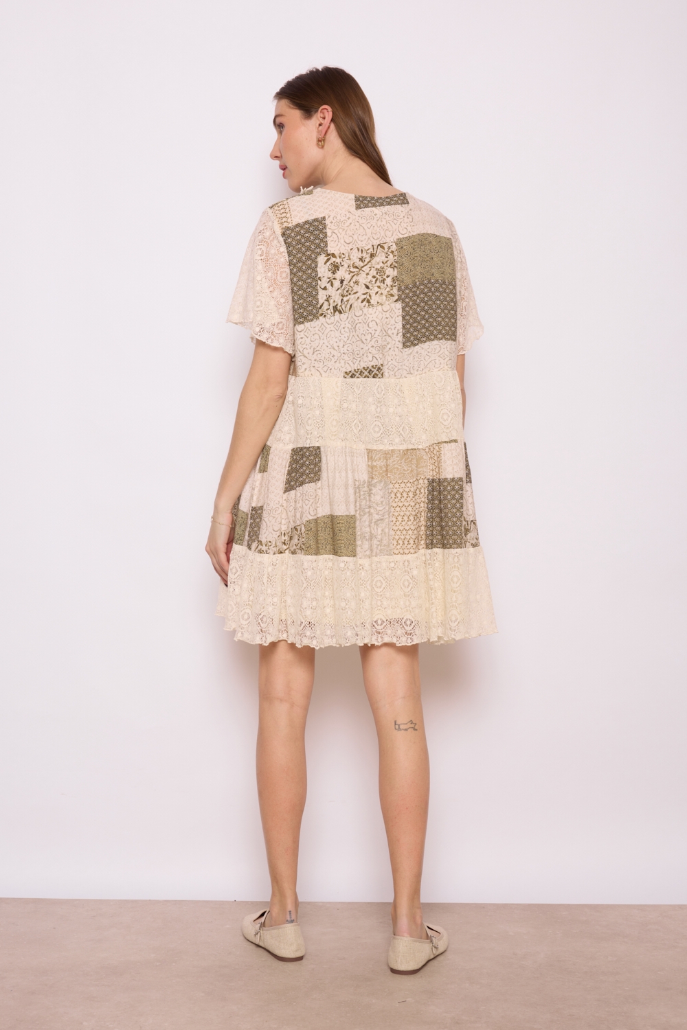 Réf. 41002 - Robe en dentelle patchwork, combinant différentes textures et motif dans des couleurs neutres. Décolleté plongeant en V et des manches courtes légèrement évasées, elle dégage un charme bohème et féminin. La robe s'évase en une jupe ample à volants, ce qui crée une silhouette gracieuse et aérienne. C'est une tenue parfaite pour les événements printaniers ou estivaux, alliant élégance et confort.