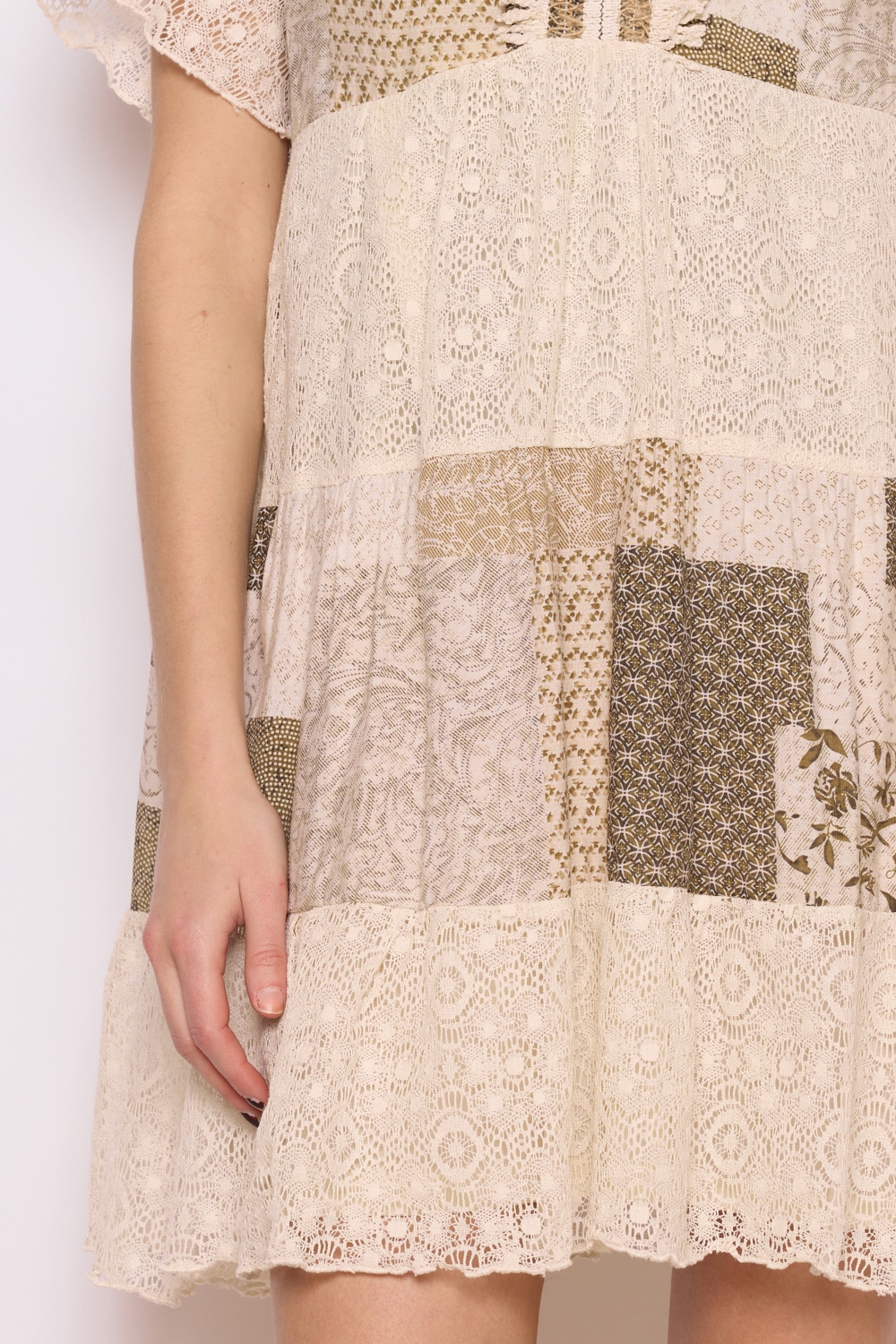 Réf. 41002 - Robe en dentelle patchwork, combinant différentes textures et motif dans des couleurs neutres. Décolleté plongeant en V et des manches courtes légèrement évasées, elle dégage un charme bohème et féminin. La robe s'évase en une jupe ample à volants, ce qui crée une silhouette gracieuse et aérienne. C'est une tenue parfaite pour les événements printaniers ou estivaux, alliant élégance et confort.