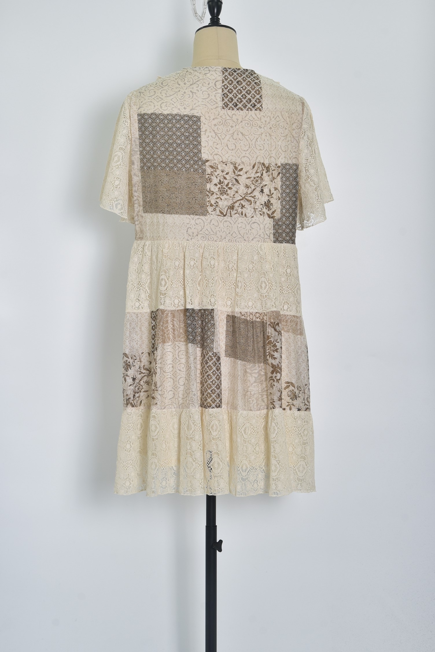 Réf. 41002 - Robe en dentelle patchwork, combinant différentes textures et motif dans des couleurs neutres. Décolleté plongeant en V et des manches courtes légèrement évasées, elle dégage un charme bohème et féminin. La robe s'évase en une jupe ample à volants, ce qui crée une silhouette gracieuse et aérienne. C'est une tenue parfaite pour les événements printaniers ou estivaux, alliant élégance et confort.