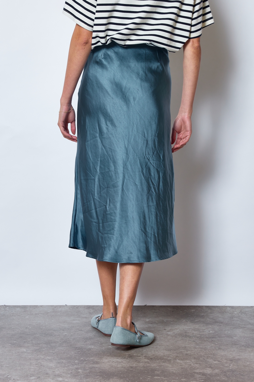 Réf. 41051B - Jupe longueur midi à la coupe évasée. Taille plate sans ceinture apparente pour un fini épuré. Matière satinée offrant un tombé souple et élégant. Fermeture discrète sur le côté.