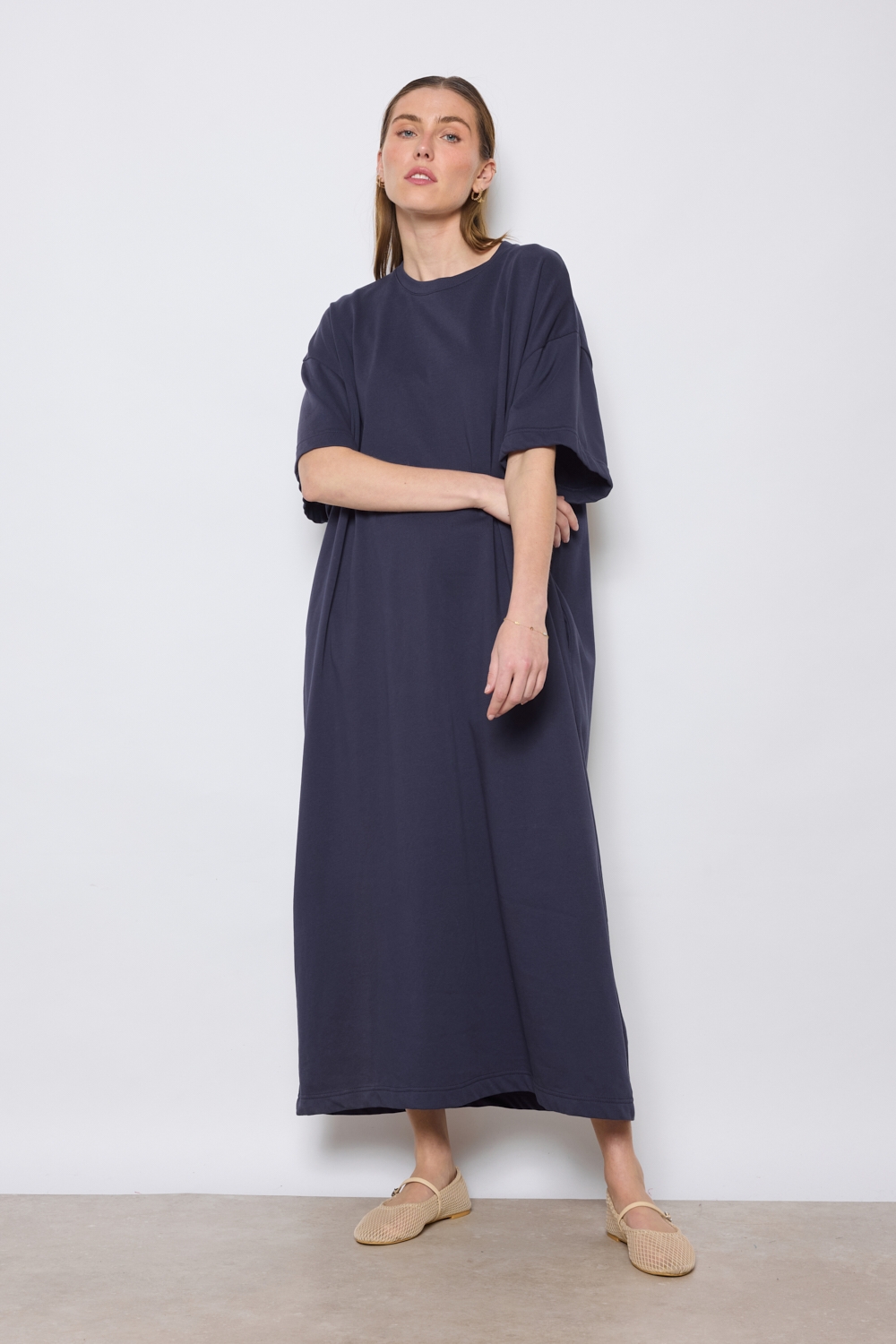 Réf. 43015B - Robe t-shirt de couleur marine. La robe a des manches courtes, une encolure ronde, poches sur les côtés et une coupe droite qui tombe de manière décontractée sur le corps. Sa simplicité est soulignée par l'absence de motif ou de détails superflus, ce qui en fait une pièce versatile qui pourrait être accessoirisée de diverses manières.