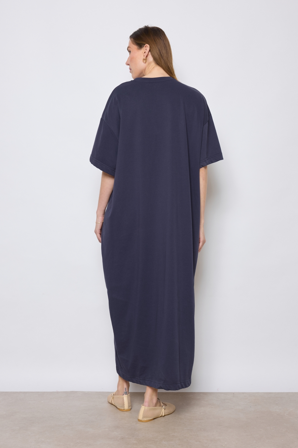 Réf. 43015B - Robe t-shirt de couleur marine. La robe a des manches courtes, une encolure ronde, poches sur les côtés et une coupe droite qui tombe de manière décontractée sur le corps. Sa simplicité est soulignée par l'absence de motif ou de détails superflus, ce qui en fait une pièce versatile qui pourrait être accessoirisée de diverses manières.