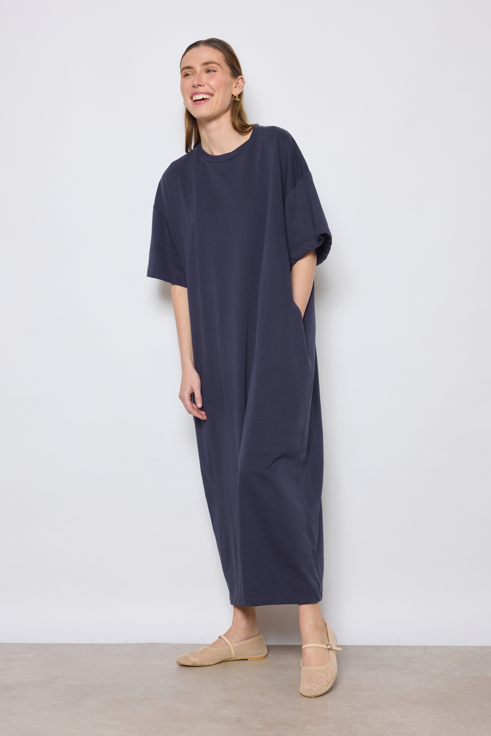 Réf. 43015B - Robe t-shirt de couleur marine. La robe a des manches courtes, une encolure ronde, poches sur les côtés et une coupe droite qui tombe de manière décontractée sur le corps. Sa simplicité est soulignée par l'absence de motif ou de détails superflus, ce qui en fait une pièce versatile qui pourrait être accessoirisée de diverses manières.